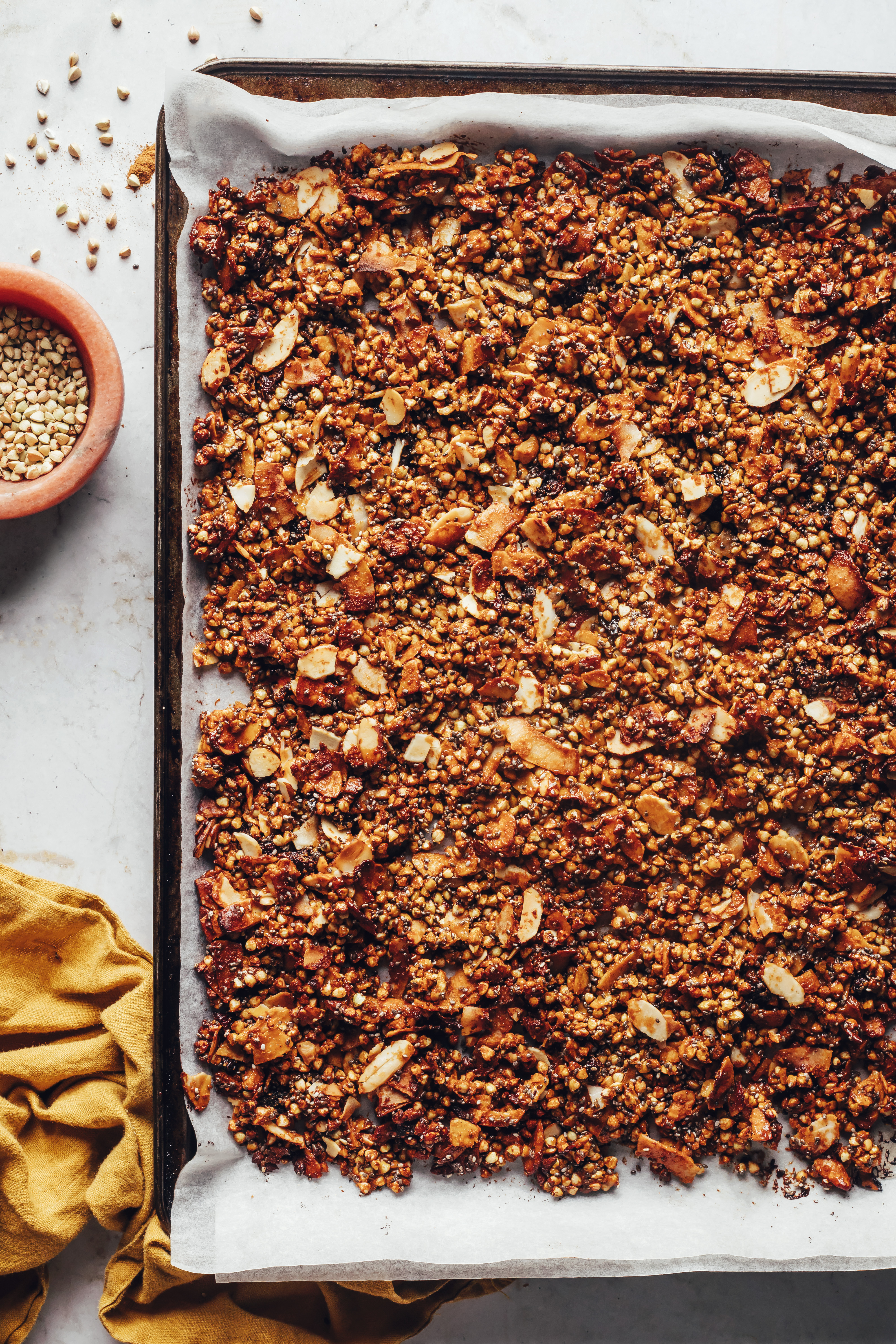 Small bowl of buckwheat next to a baking tray of gluten-free granola