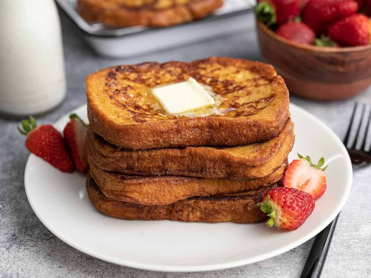Side view of four slices of french toast stacked on a white plate.